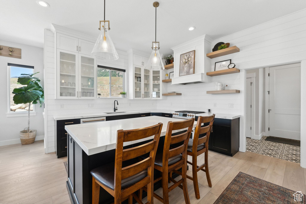 Kitchen featuring decorative light fixtures, light wood-type flooring, a kitchen island, sink, and white cabinets