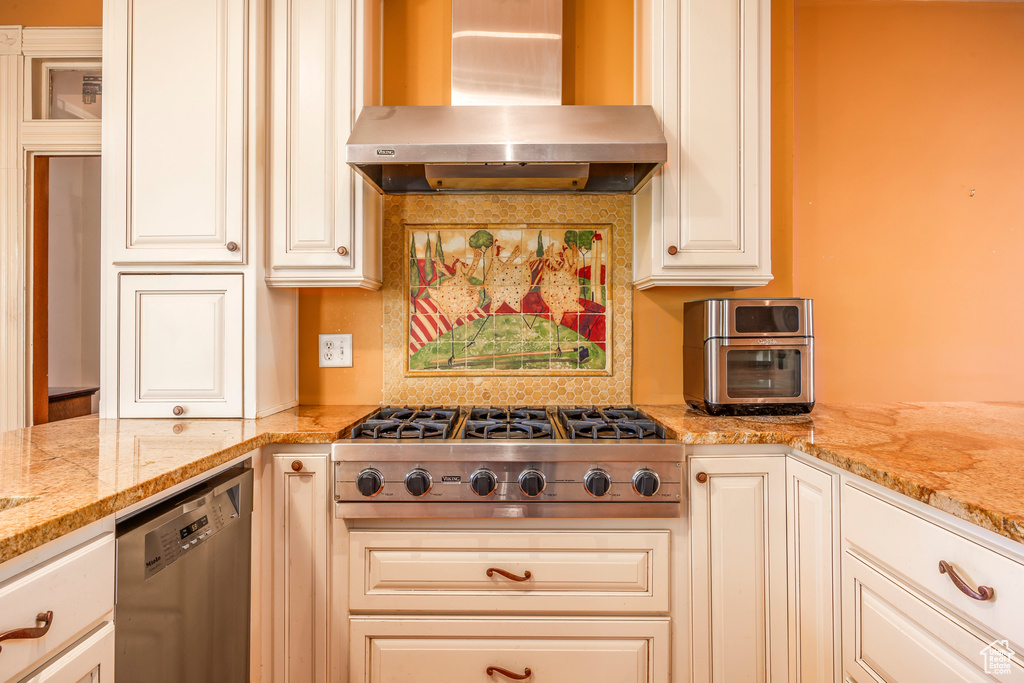 Kitchen with wall chimney exhaust hood, white cabinets, and appliances with stainless steel finishes