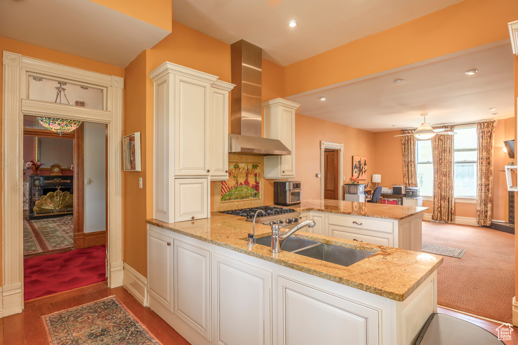 Kitchen featuring wall chimney exhaust hood, carpet floors, kitchen peninsula, and sink