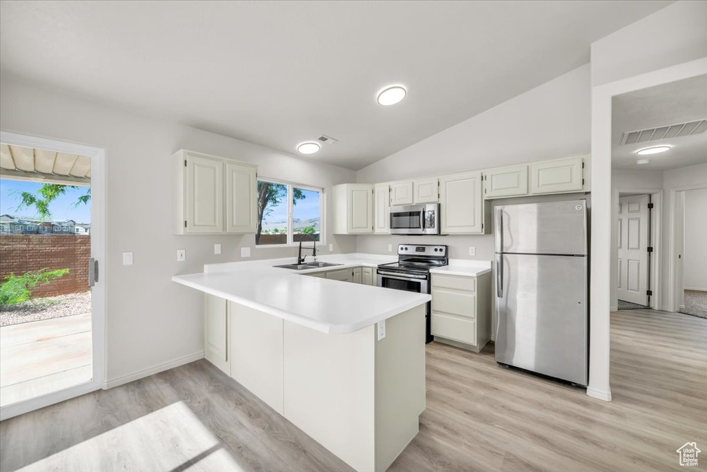 Kitchen featuring light hardwood / wood-style flooring, kitchen peninsula, stainless steel appliances, vaulted ceiling, and sink