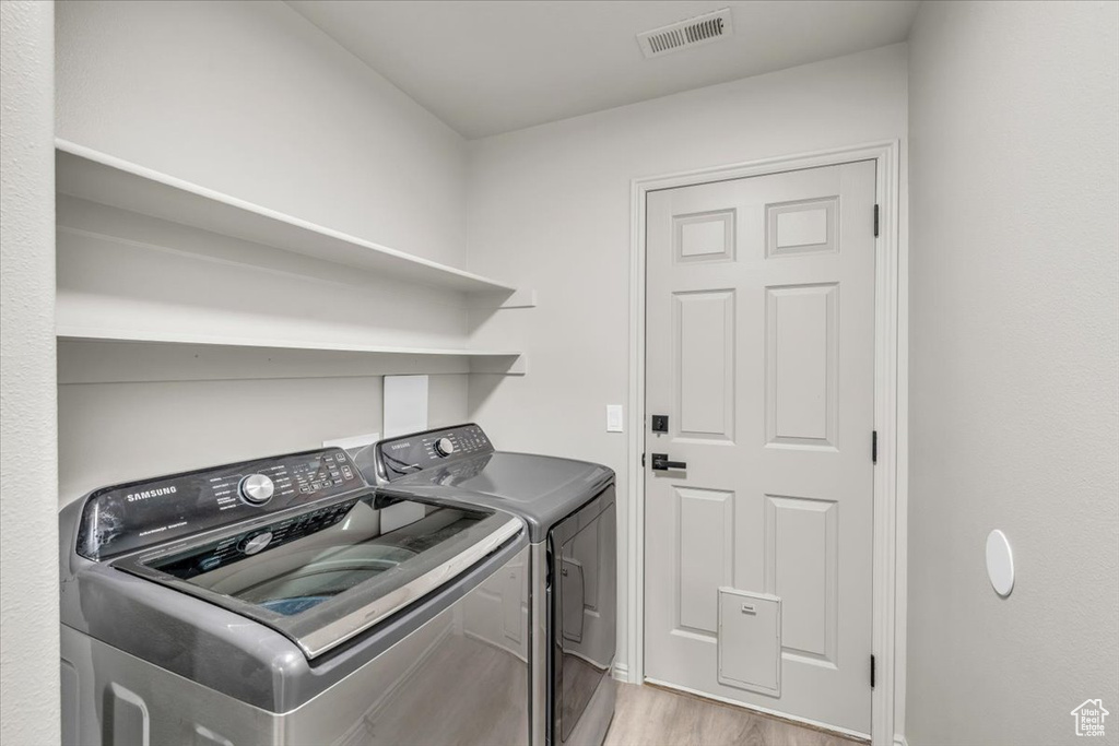 Laundry room with washer and clothes dryer and light hardwood / wood-style flooring