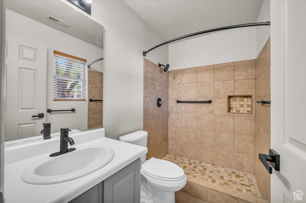 Bathroom featuring a tile shower, toilet, and vanity