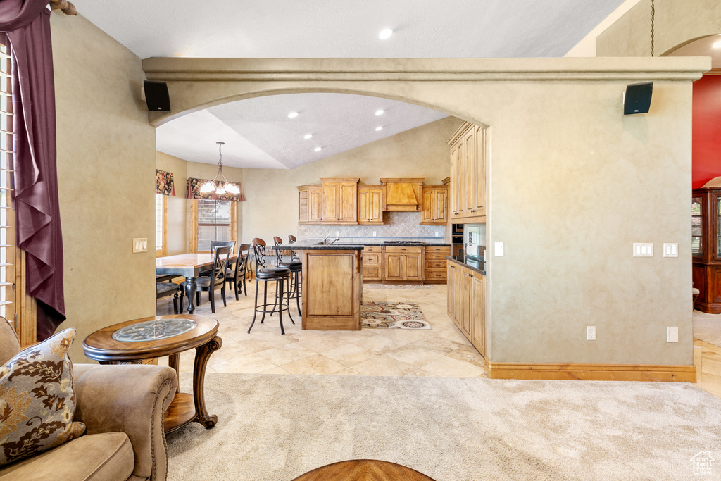 Kitchen with tasteful backsplash, pendant lighting, premium range hood, light colored carpet, and lofted ceiling