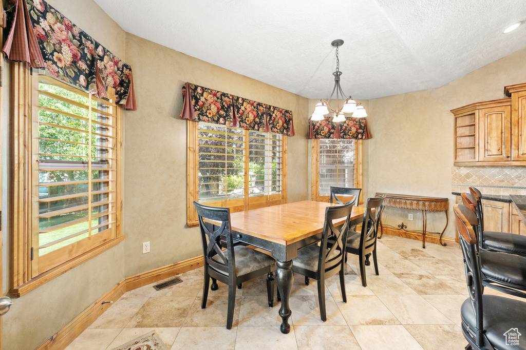 Tiled dining room with a chandelier, a textured ceiling, and vaulted ceiling