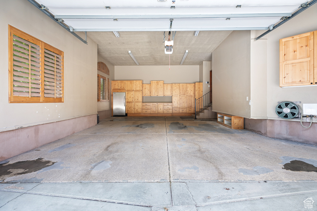 Garage featuring a garage door opener and stainless steel fridge