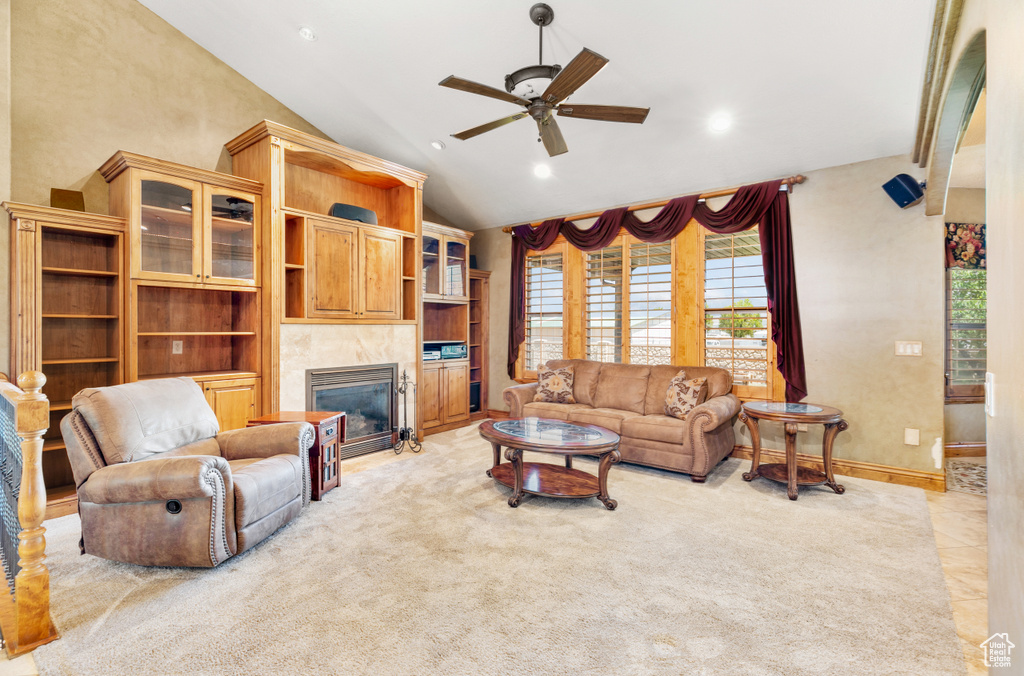 Living room featuring a tiled fireplace, ceiling fan, light tile floors, and lofted ceiling