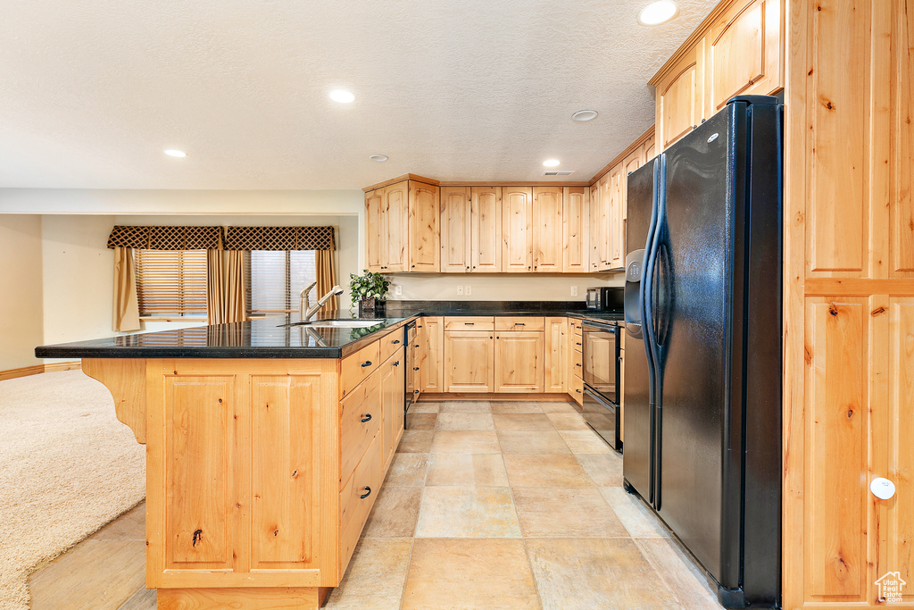 Kitchen featuring light brown cabinetry, black fridge, a kitchen breakfast bar, range with electric cooktop, and sink