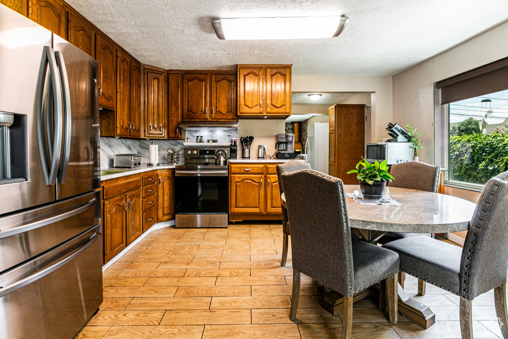 Kitchen featuring backsplash, appliances with stainless steel finishes, light hardwood / wood-style flooring, and a textured ceiling