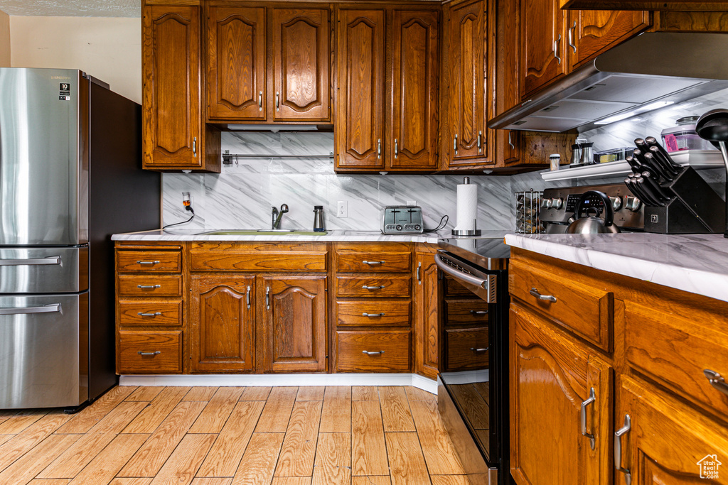 Kitchen featuring light hardwood / wood-style flooring, range with electric cooktop, stainless steel refrigerator, sink, and tasteful backsplash