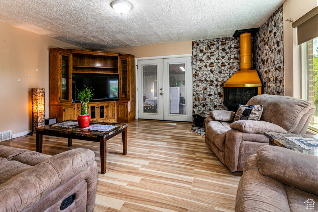 Living room featuring light hardwood / wood-style floors, french doors, a wood stove, and a textured ceiling