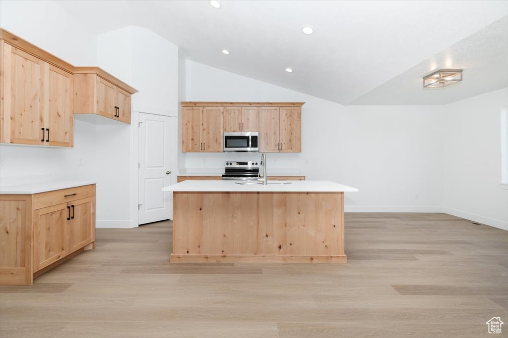 Kitchen featuring light brown cabinets, a center island with sink, stainless steel appliances, and lofted ceiling