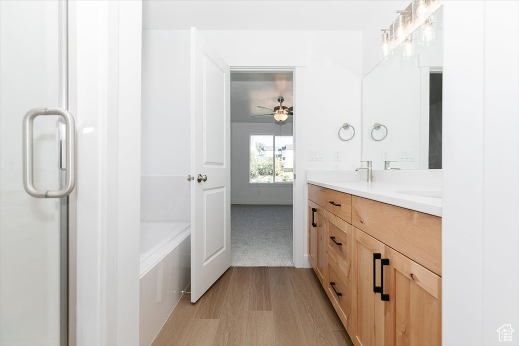 Bathroom with wood-type flooring, a tub, vanity, and ceiling fan