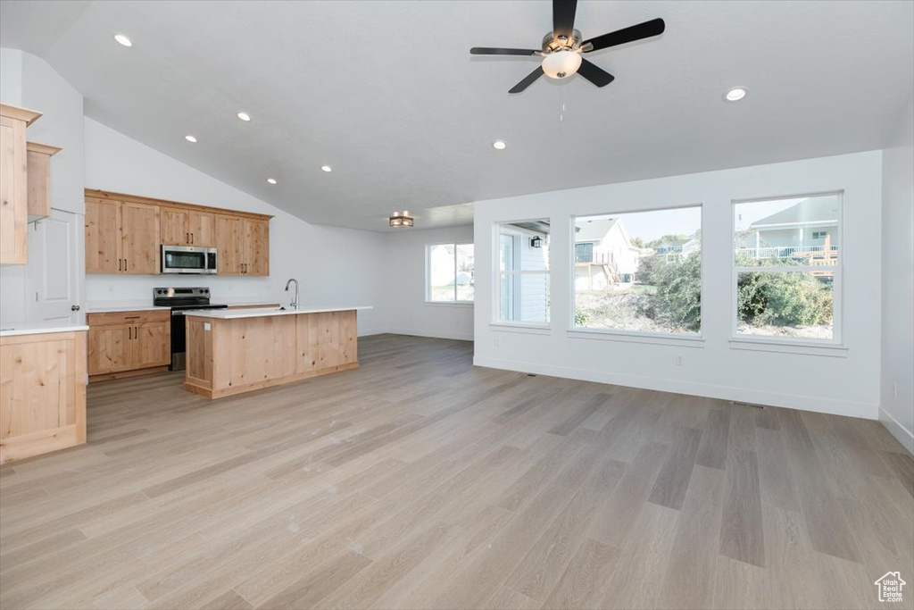 Kitchen with appliances with stainless steel finishes, light hardwood / wood-style floors, light brown cabinetry, ceiling fan, and a kitchen island with sink