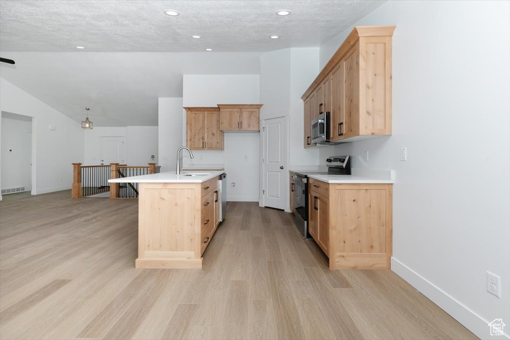 Kitchen with a textured ceiling, a kitchen island with sink, light hardwood / wood-style flooring, stainless steel appliances, and light brown cabinets