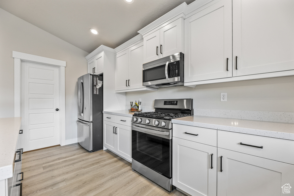 Kitchen with light stone countertops, light hardwood / wood-style flooring, vaulted ceiling, white cabinets, and appliances with stainless steel finishes