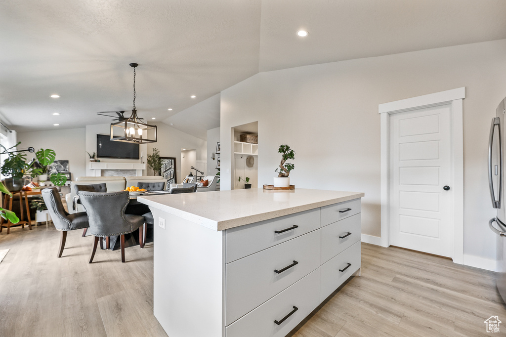 Kitchen with light hardwood / wood-style floors, hanging light fixtures, lofted ceiling, a kitchen island, and white cabinets