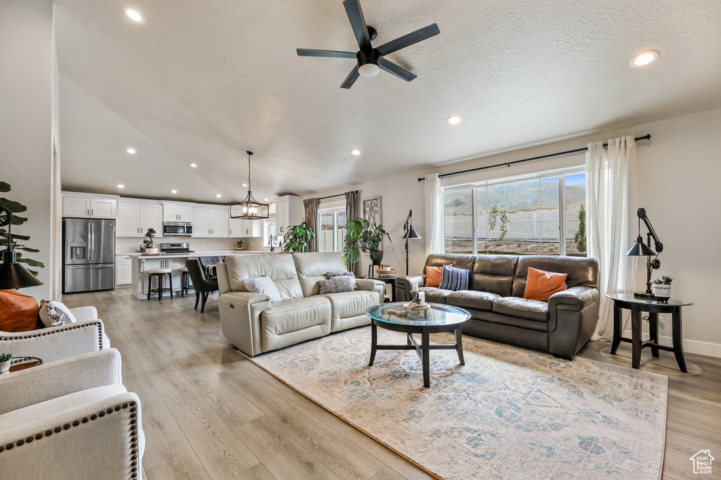 Living room with high vaulted ceiling, a textured ceiling, ceiling fan, and light hardwood / wood-style flooring