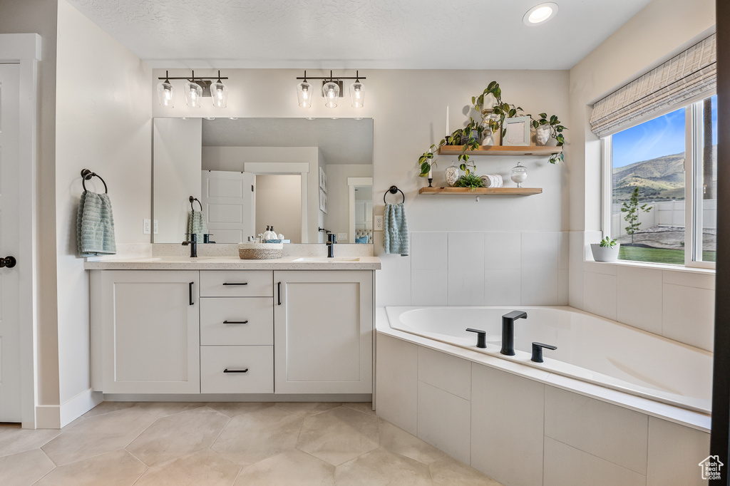 Bathroom with vanity with extensive cabinet space, tiled tub, a textured ceiling, and tile floors