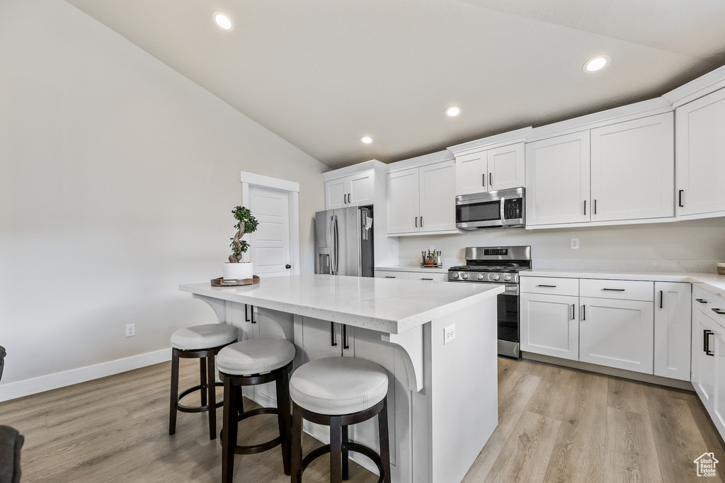 Kitchen featuring appliances with stainless steel finishes, light hardwood / wood-style floors, white cabinets, and vaulted ceiling