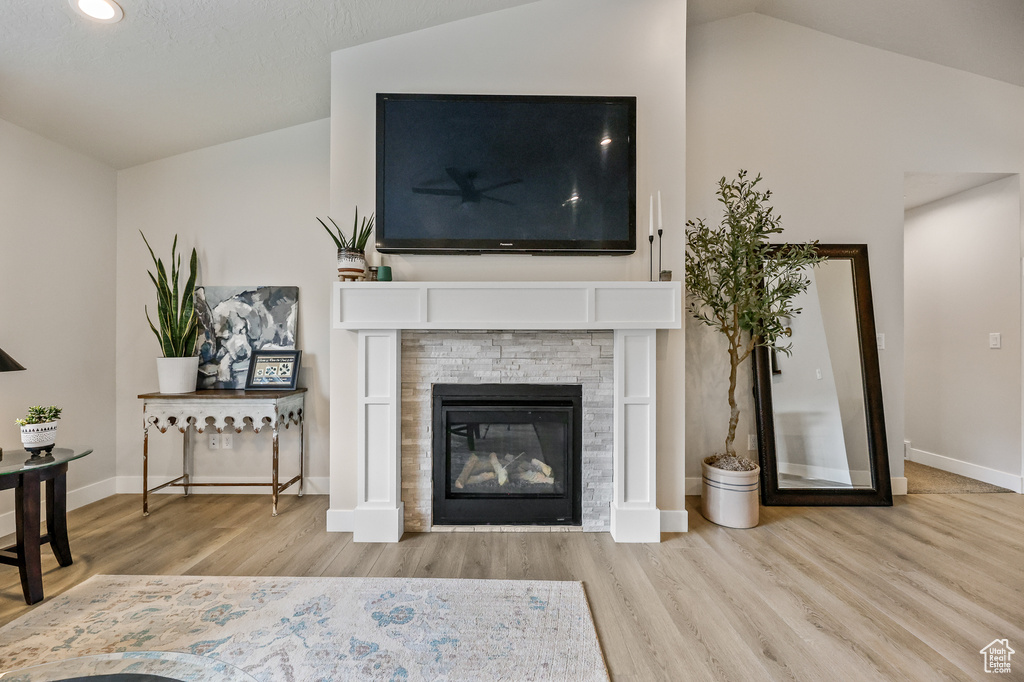 Living room with a stone fireplace, light hardwood / wood-style floors, and lofted ceiling