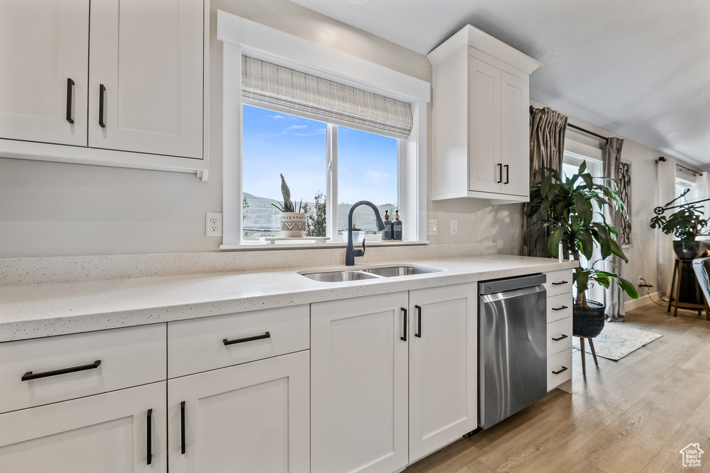 Kitchen featuring white cabinetry, light wood-type flooring, light stone counters, sink, and dishwasher