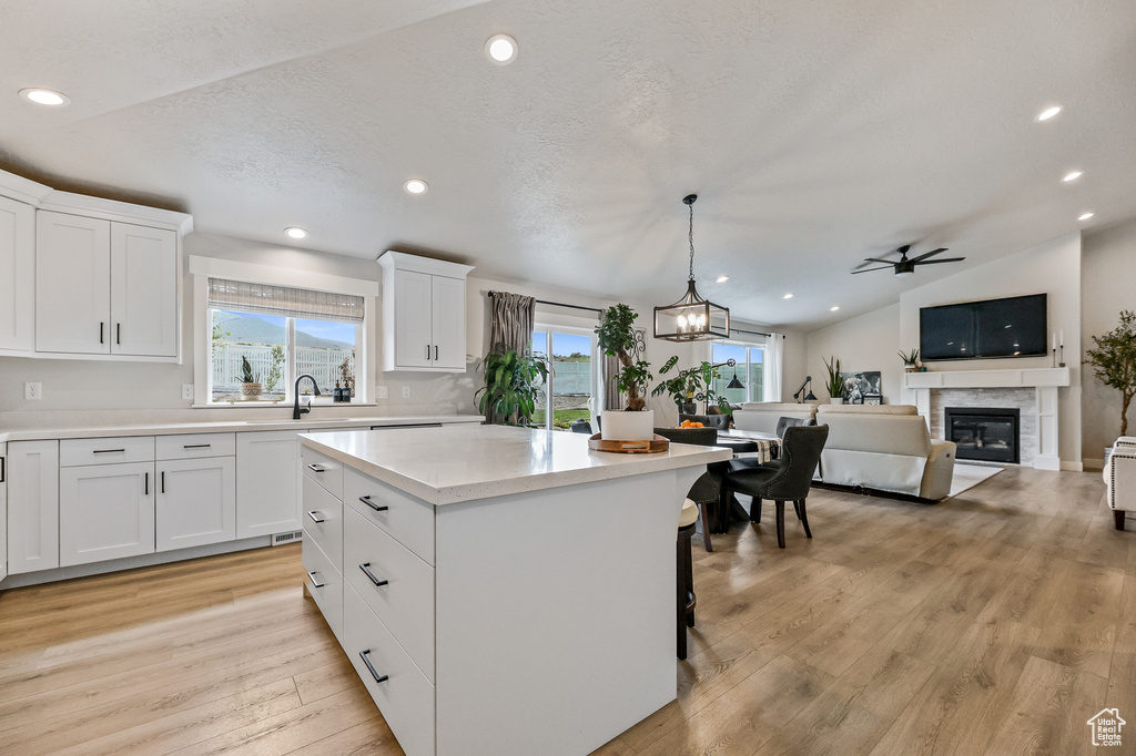 Kitchen featuring a center island, hanging light fixtures, lofted ceiling, light wood-type flooring, and white cabinets