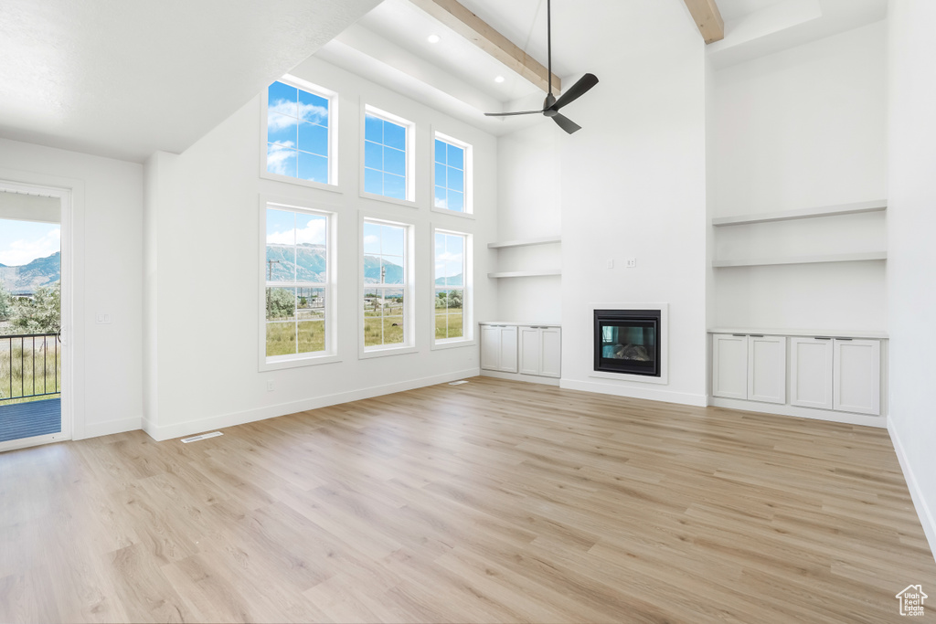 Unfurnished living room featuring ceiling fan, beam ceiling, light hardwood / wood-style flooring, and a towering ceiling