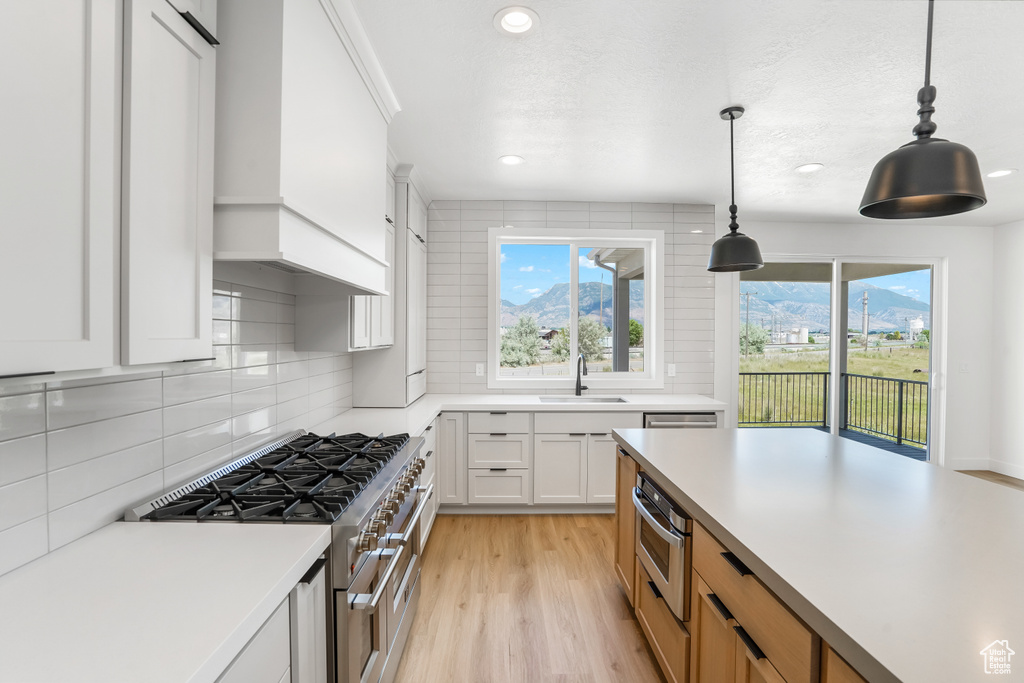 Kitchen featuring stainless steel appliances, tasteful backsplash, white cabinetry, light wood-type flooring, and pendant lighting