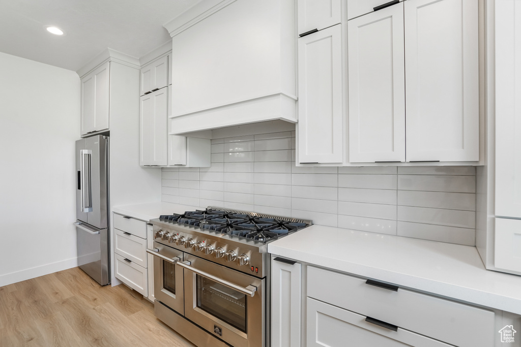 Kitchen featuring high end appliances, light hardwood / wood-style floors, white cabinets, and tasteful backsplash