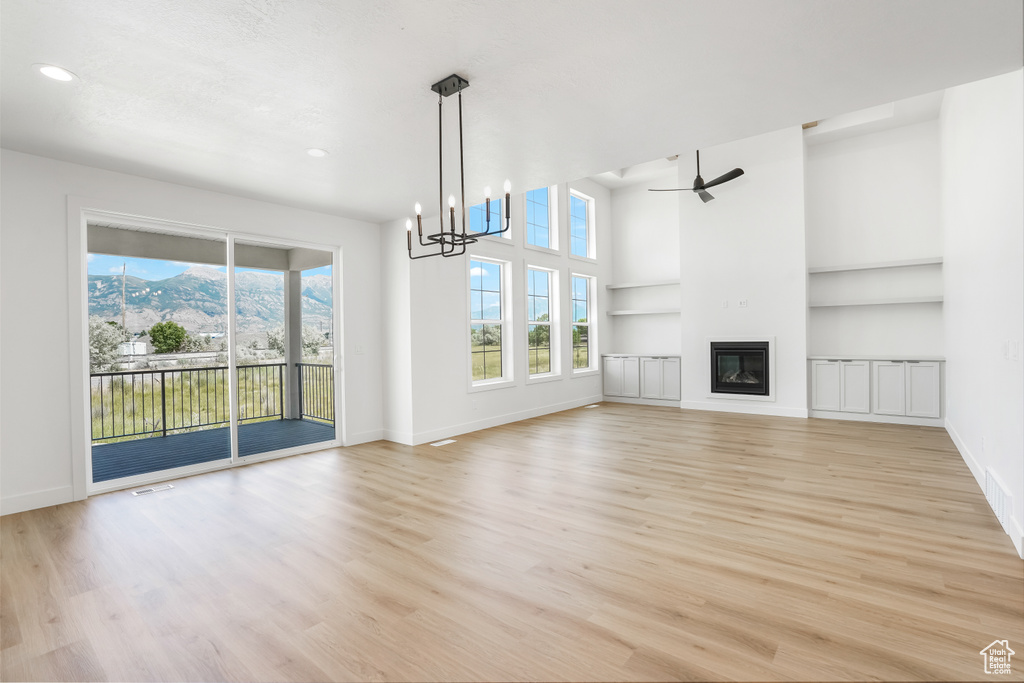 Unfurnished living room with light hardwood / wood-style floors, a towering ceiling, a mountain view, and ceiling fan with notable chandelier