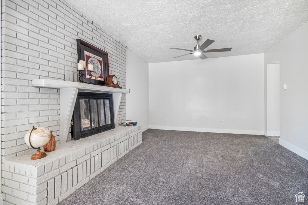 Unfurnished living room with a textured ceiling, a fireplace, carpet flooring, and ceiling fan