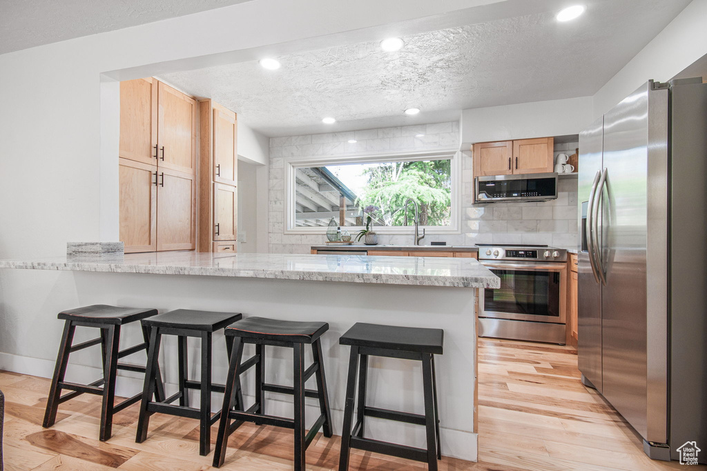 Kitchen featuring light hardwood / wood-style flooring, stainless steel appliances, tasteful backsplash, light stone countertops, and a textured ceiling