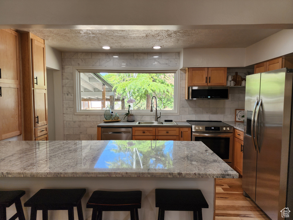 Kitchen featuring tasteful backsplash, light wood-type flooring, a textured ceiling, sink, and appliances with stainless steel finishes