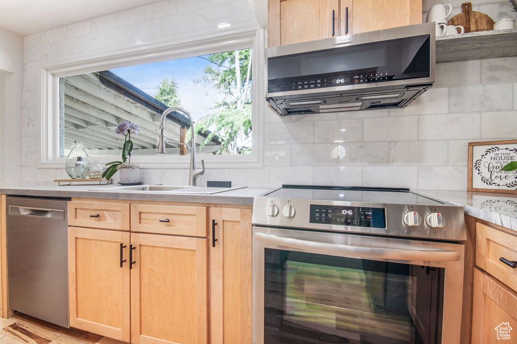 Kitchen featuring light brown cabinetry, tasteful backsplash, appliances with stainless steel finishes, sink, and range hood