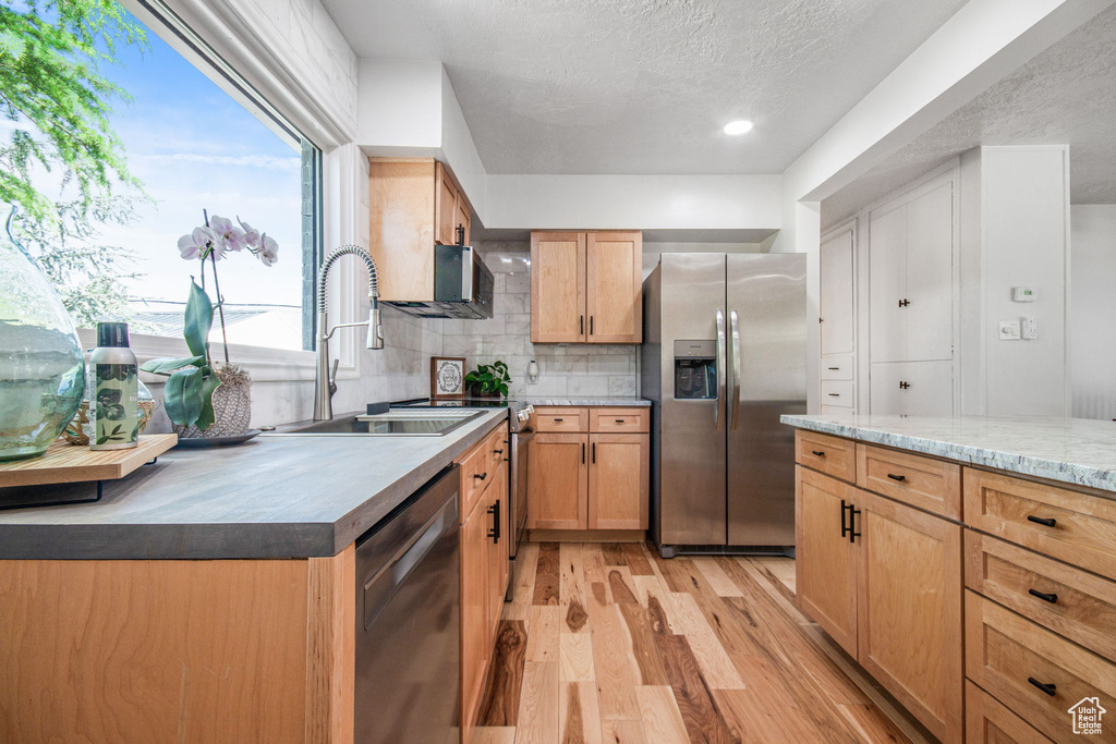 Kitchen featuring stainless steel refrigerator with ice dispenser, backsplash, dishwasher, light wood-type flooring, and sink