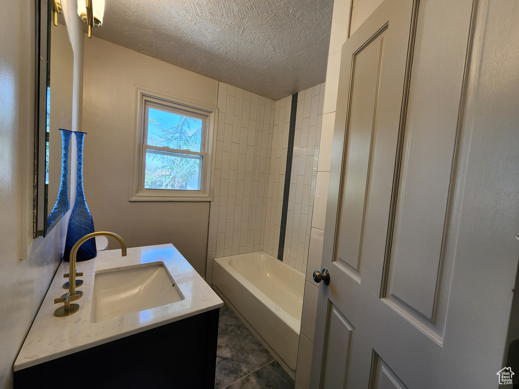 Bathroom with vanity with extensive cabinet space, tile flooring, tiled shower / bath combo, and a textured ceiling