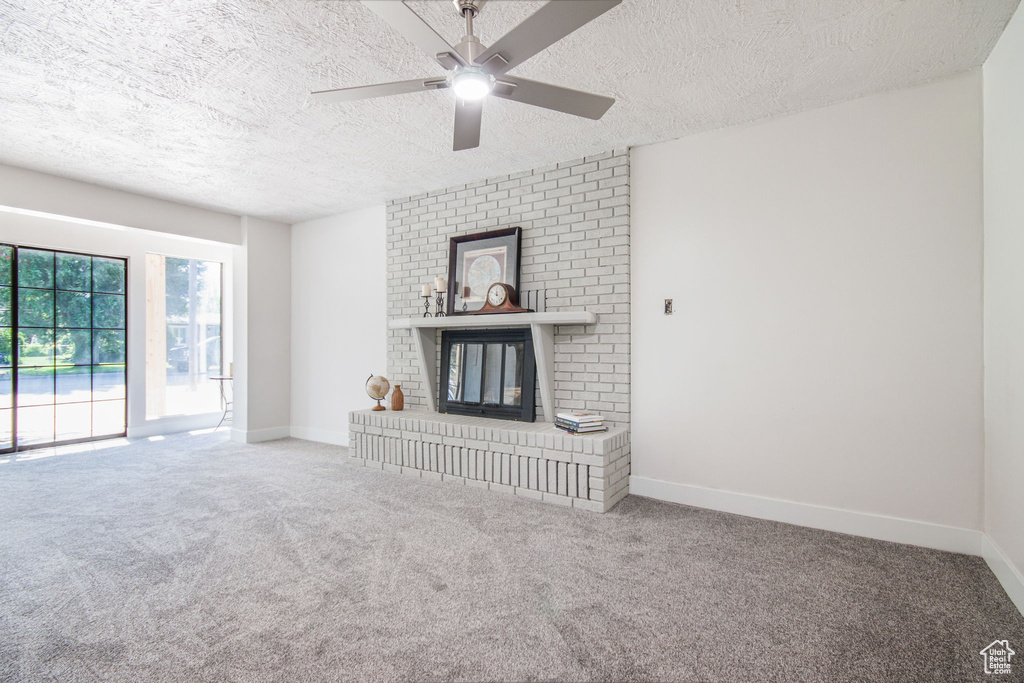 Unfurnished living room featuring brick wall, a brick fireplace, ceiling fan, carpet floors, and a textured ceiling