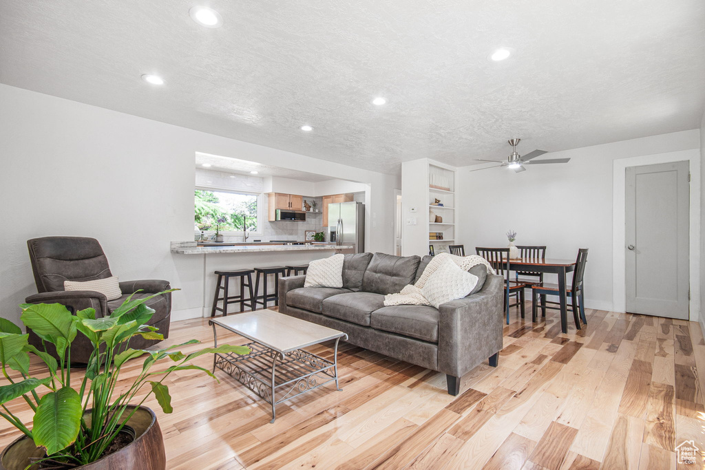 Living room featuring ceiling fan, a textured ceiling, and light wood-type flooring