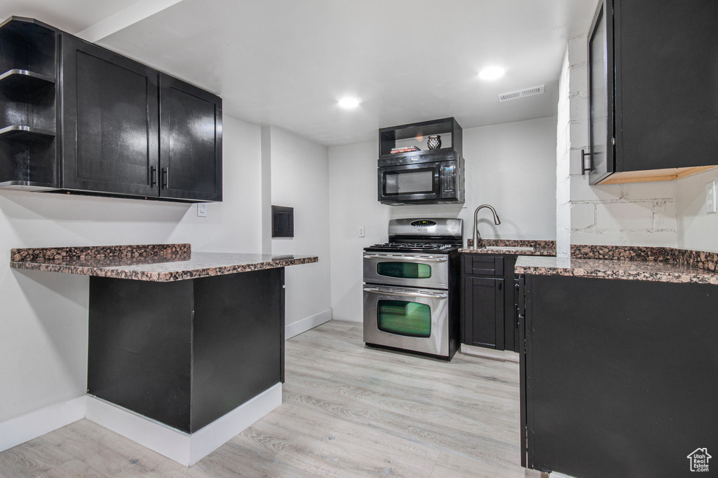 Kitchen with dark stone counters, light hardwood / wood-style floors, kitchen peninsula, range with two ovens, and sink