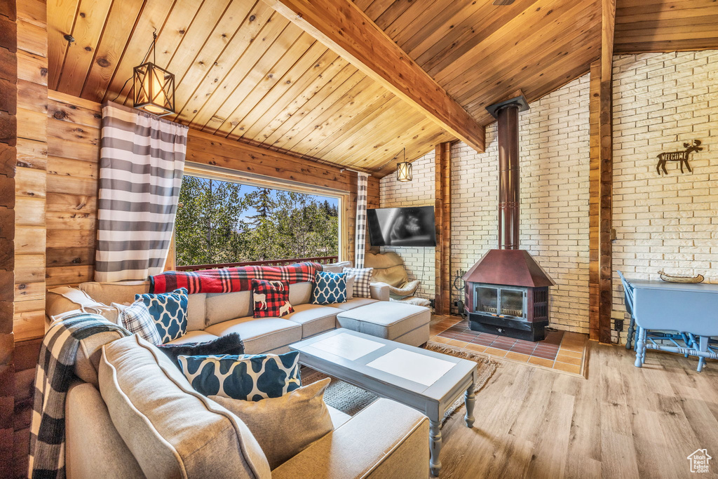 Living room with hardwood / wood-style flooring, lofted ceiling with beams, brick wall, and a wood stove