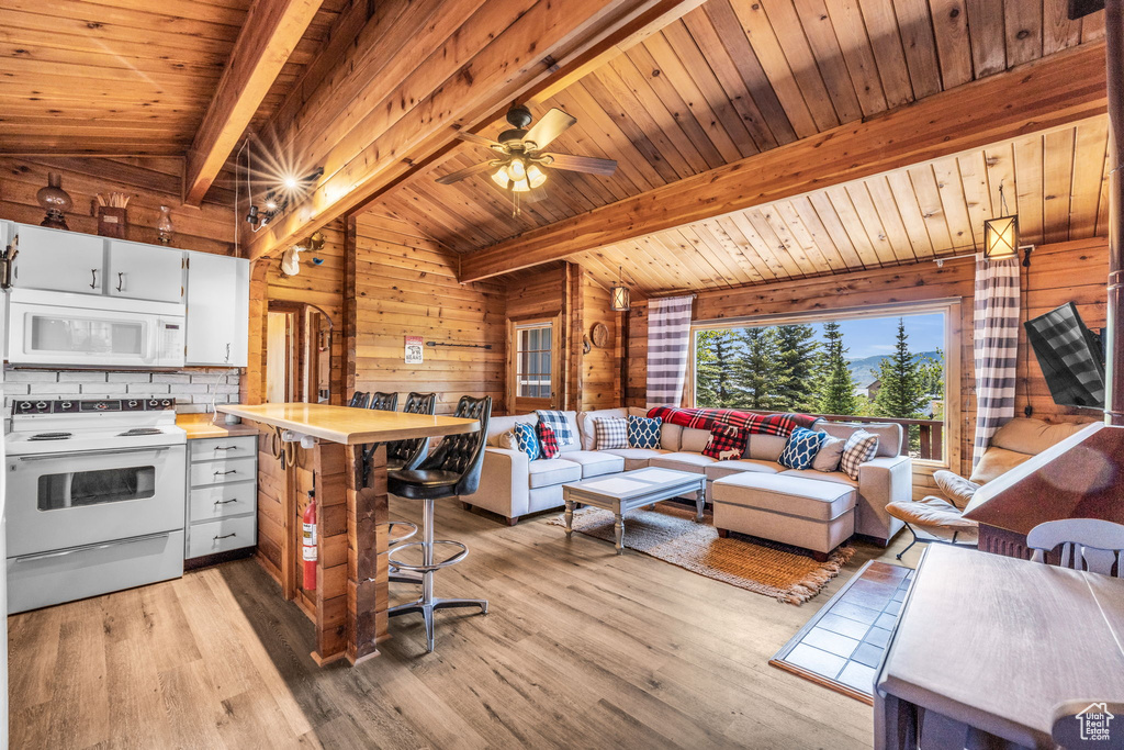 Living room featuring ceiling fan, vaulted ceiling with beams, light wood-type flooring, wood ceiling, and wooden walls