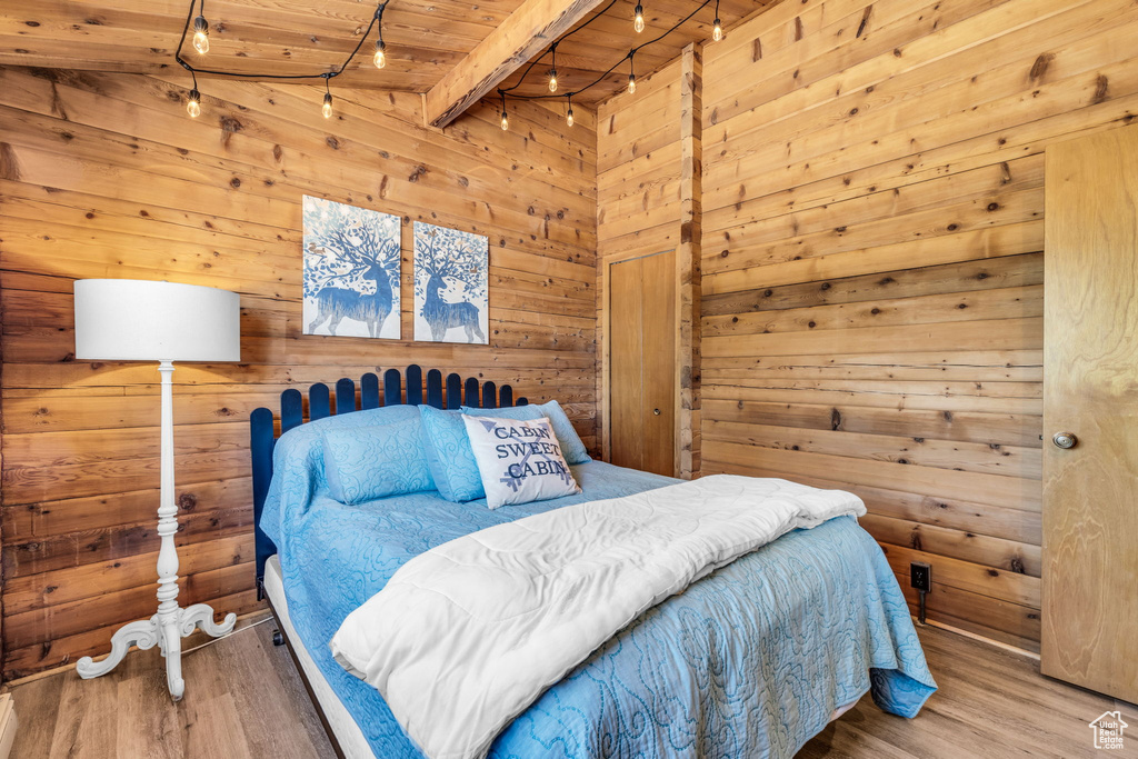 Bedroom featuring beamed ceiling, wooden walls, light hardwood / wood-style floors, and wood ceiling