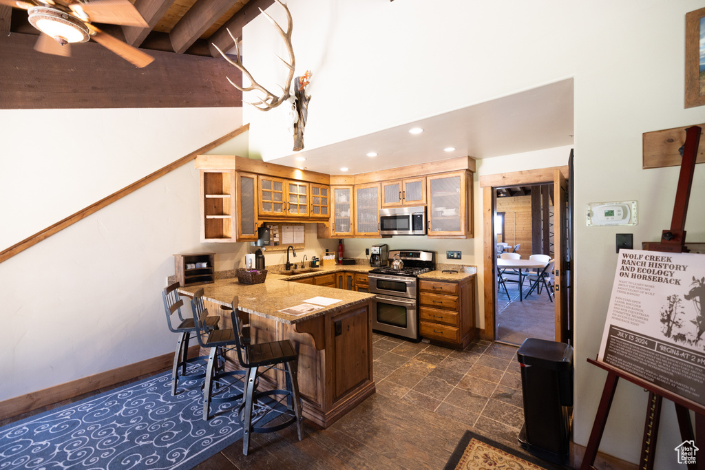 Kitchen with appliances with stainless steel finishes, kitchen peninsula, a kitchen bar, ceiling fan, and dark tile floors