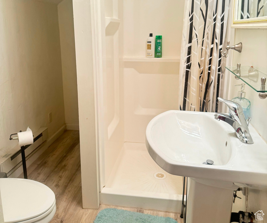 Bathroom with curtained shower, a baseboard heating unit, hardwood / wood-style flooring, and toilet