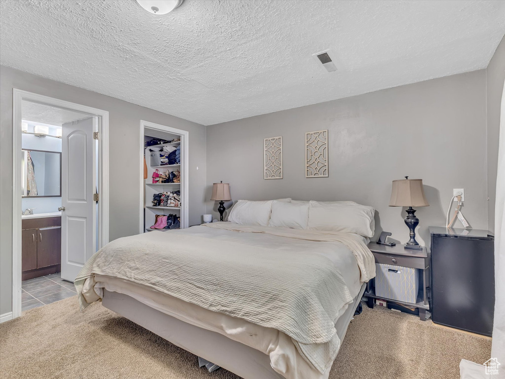 Carpeted bedroom with connected bathroom, a closet, a textured ceiling, and a walk in closet