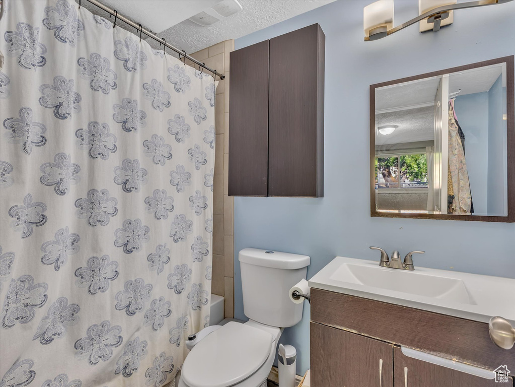 Full bathroom featuring shower / bath combination with curtain, vanity, toilet, and a textured ceiling