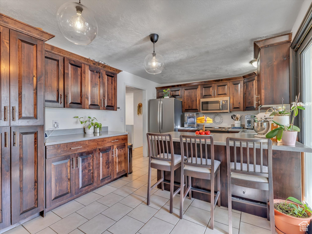 Kitchen featuring stainless steel appliances, a breakfast bar area, light tile floors, and decorative light fixtures