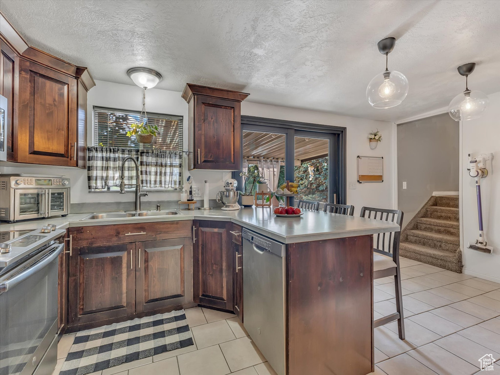 Kitchen featuring kitchen peninsula, hanging light fixtures, appliances with stainless steel finishes, sink, and light tile floors