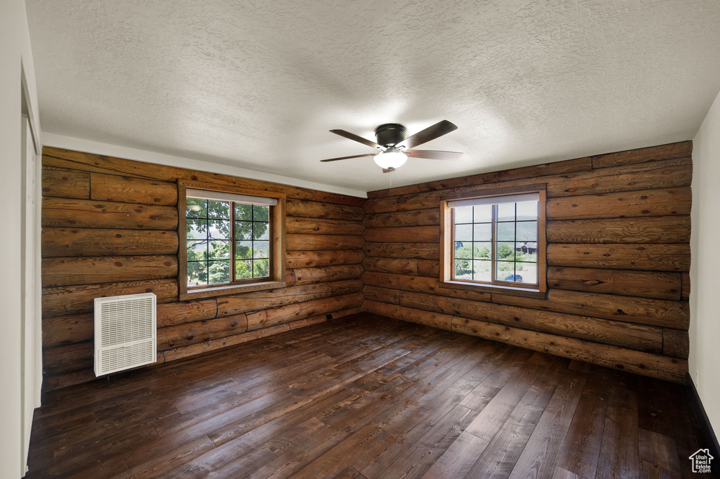 Spare room with a textured ceiling, dark hardwood / wood-style floors, ceiling fan, and log walls