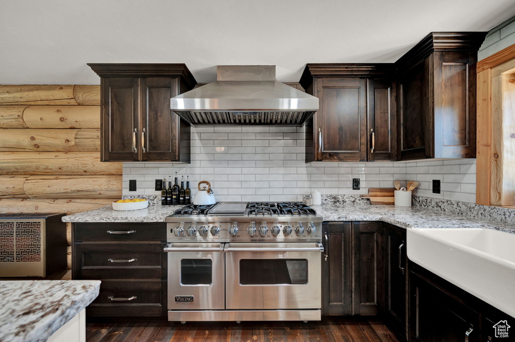 Kitchen with double oven range, wall chimney range hood, dark wood-type flooring, and backsplash